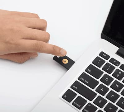 A person placing a finger on a YubiKey, a type of passkey, to sign in to an SSO service